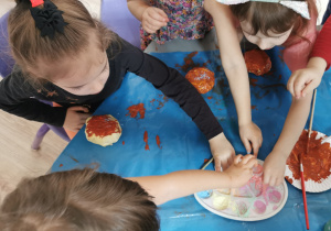 Dziewczynki dekorują pomalowane pączki posypką.