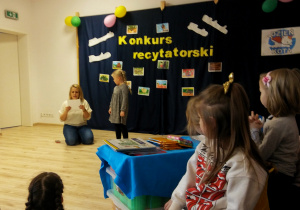 Dziewczynka recytuje wiersz przed publicznością.