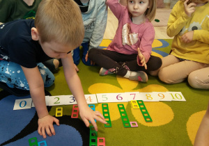 Dzieci siedzą w kole i uczestniczą w zabawie matematycznej z Klockami Nemi.