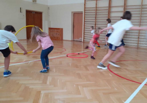 Dzieci biorą udział w wyścigu rzędów z obręczami (uczniowie podstawówki pomagają dziewczynkom przejść przez obręcze).