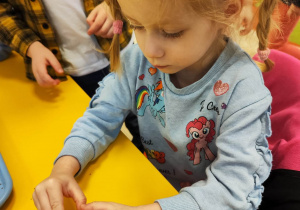 Dziewczynka przykleja plastikowe oczka do żółtego, plastikowego jajka z Kinder Niespodzianki.