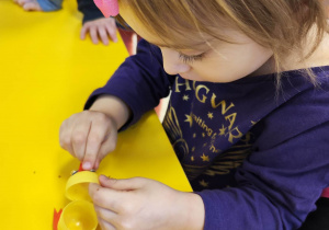 Dziewczynka przykleja plastikowe oczka do żółtego, plastikowego jajka z Kinder Niespodzianki.