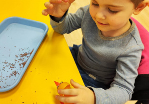 Chłopiec przykleja plastikowe oczka do żółtego, plastikowego jajka z Kinder Niespodzianki.