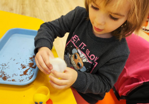 Dziewczynka wkłada watę do plastikowego jajka z Kinder Niespodzianki.