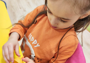 Dziewczynka przykleja plastikowe oczka do żółtego, plastikowego jajka z Kinder Niespodzianki.