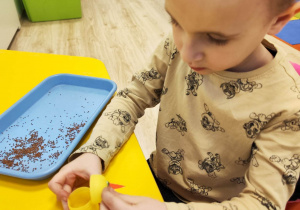 Chłopiec przykleja plastikowe oczka do żółtego, plastikowego jajka z Kinder Niespodzianki.