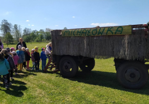 Dzieci wchodzą po drewnianej drabince na drewnianą przyczepę.