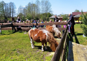 Dzieci, wraz z nauczycielkami, jadą drewnianą przyczepą ciągniętą przez traktor.