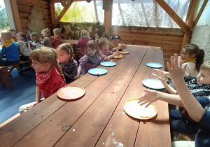 Warsztaty "Od ziarenka do bochenka". Dzieci siedzą przy stolach. Przed nimi leżą plastikowe talerzyki oprószone mąką.