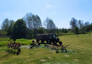 Dzieci, wraz z nauczycielkami, jadą drewnianą przyczepą ciągniętą przez traktor.