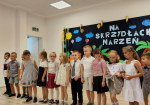 Sala gimnastyczna. Występ z okazji zakończenia roku. W tle dekoracja.