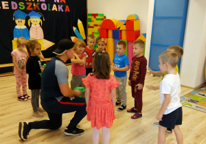 Zajęcia pokazowe z piłki nożnej. Dzieci stoją w kole i słuchają trenera.