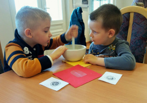 Lekcja muzealna. Dwóch chłopców rozkrusza kostki cukru w moździerzu.