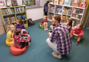 Zajęcia w bibliotece. Dzieci siedzą na pufach i słuchają pana bibliotekarza.