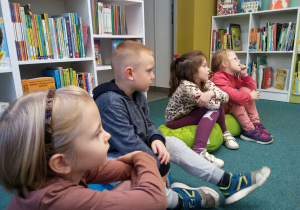 Dzieci siedzą na pufach i oglądają teatrzyk.