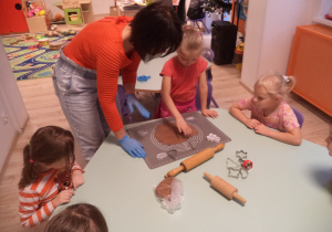 Dziewczynka wraz z pomocą Pani Ewy wałkuje ciasta na pierniki