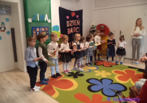 Przedszkolaki z grupy Motylków trzymają w rękach własnoręcznie przygotowane laurki oraz ramki ze zdjęciami, które wręczą swoim Babciom i Dziadkom. Na zdjęciu obok dzieci jest również Pani Marta - nauczycielka grupy Motylków