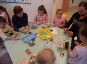 Dzieci wraz z dorosłymi przygotowują wielkanocne dekoracje.