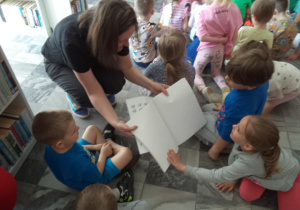 Pani bibilotekarka pokazuje dzieciom książkę napisaną alfabetem Braille'a.