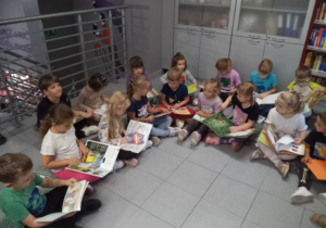 Dzieci siedzą na podłodze i oglądają kolorowe książki.