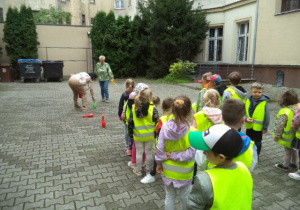 Dzieci stoją w dwóch rzędach. Przed nimi panie układają kręgle.