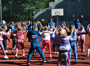 Boisko szkolne. Grupa dzieci naśladuje instruktorów podczas rozgrzewki.