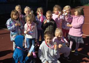 Boisko szkolne. Dzieci z grupy Biedronek pozują z medalami.