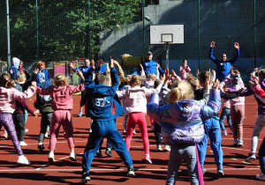 Boisko szkolne. Grupa dzieci naśladuje instruktorów podczas rozgrzewki.