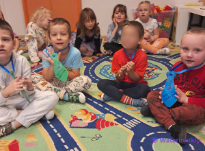 Chłopcy siedzą na dywanie i pozują z kolorowymi krawatami.