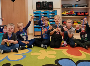 Grupa uśmiechniętych chłopców pozuje do zdjęcia z medalami i lizakami.