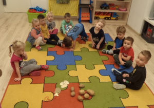 Grupa dzieci siedzi na dywanie. Przed nimi leżą ziemniaki i medale w kształcie ziemniaków.