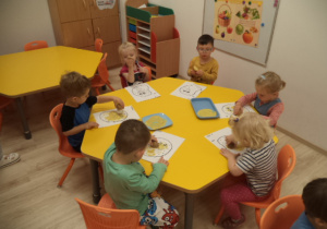 Dzieci siedzą przy stoliku. Wykonują karty pracy z ziemniakiem.