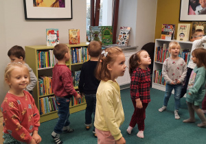 Dzieci oglądają książki na regałach oraz zabawki, w sali przeznaczonej dla dzieci.