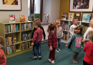 Dzieci oglądają książki na regałach oraz zabawki, w sali przeznaczonej dla dzieci.