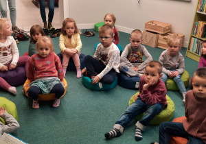 Dzieci siedzą na pufach i słuchają Pani Bibliotekarki.