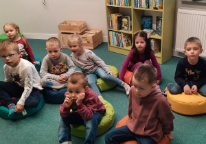 Dzieci siedzą na pufach i słuchają Pani Bibliotekarki.