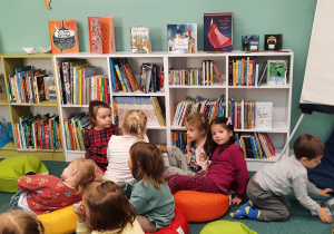 Dzieci siedzą na pufach i słuchają Pani Bibliotekarki.