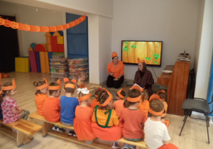 Dzieci siedzą na ławkach i oglądają film o dyni wyświetlany na tablicy multimedilnej.