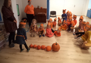 Dziewczynka ustawia dynie od największej do najmniejszej. Reszta dzieci ją obserwuje.