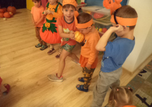 Dzieci stoją w rzędzie i podają sobie dynię.