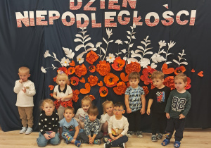 Dzieci z grupy Pszczółek pozują na tle dekoracji z okazji Dnia Niepoległości.