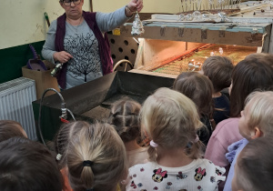 Grupa dzieci znajduje się w fabryce bombek. Pani pokazuje im jak wygląda bombka po procesie srebrzenia.