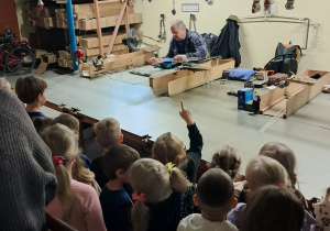 Grupa dzieci znajduje się w fabryce bombek. Obserwują one jak Pan ogrzewa szkło, aby powstała bomka.