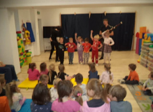 Na zdjęciu widoczna jest Pani oraz Pan grający na fagocie oraz dzieci, które tańczą krakowiaka oraz pozostałe przedszkolaki, które słuchają gry na instrumencie i oglądają taniec kolegów