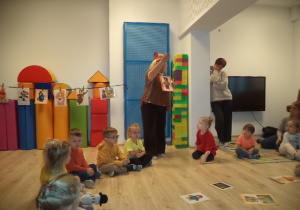 Dzieci siedzą w kole i słuchają jak pani opowiada o Misiu Uszatku.