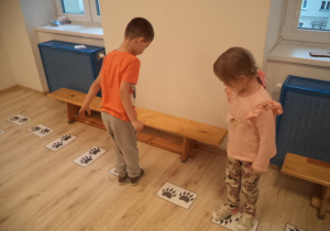 Chłopiec i dziewczynka stoją na kartach przedstawiających łapki odwrócone w różne strony.