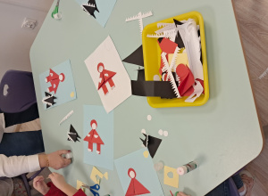 Dzieci siezą przy stoliku i tworzą pracę plastyczną - czerwonego kapturka i wilka z figur geometrycznych.