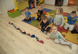 Na zdjęciu widać przedszkolaki z grupy 1, które aktywnie uczestniczą w obchodach Andrzejek. Dzieci układają buty - jeden za drugim.