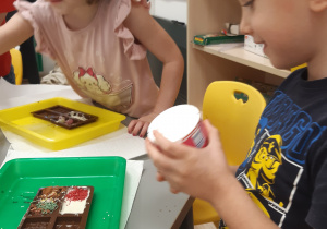 Na zdjęciu widoczny jest chłopiec i dziewczynka, którzy dekorują swoje tabliczki czekolady.