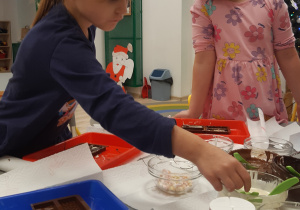 Na zdjęciu widoczne są dziewczynki wlewające czekoladę do foremek.